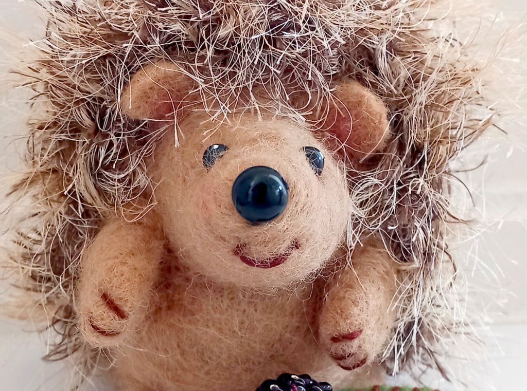 A close up of a needle felt hedgehog, with furry spines and a smiling face,