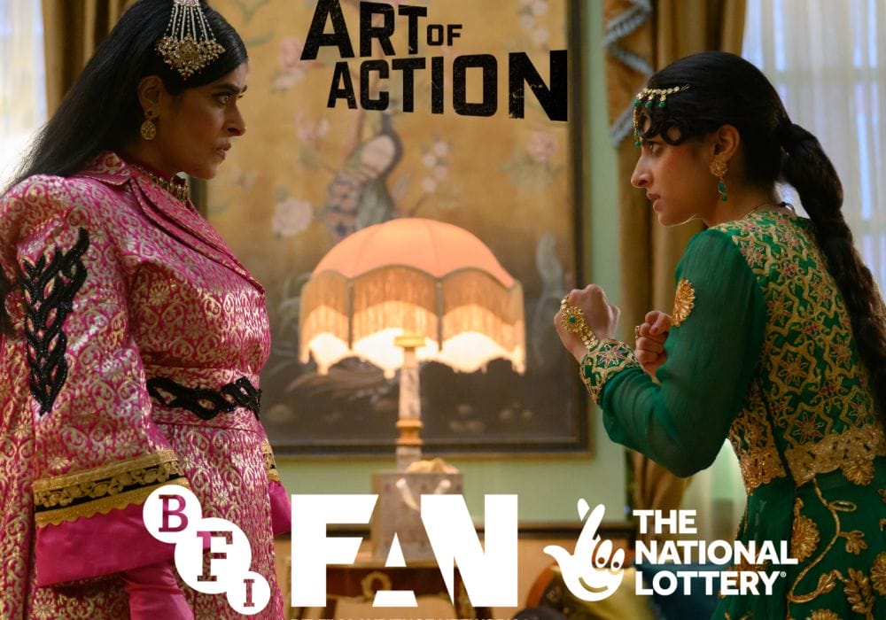 The image shows a living room, you can see curtains and wallpaper and the in the middle of the image is a lamp. To the left and the right of the image are Pakistani women. The one to the right is wearing traditional gold and green clothes, has long dark plated hair and is stood in a fight stance with both hands up as if she were punching. To the left the woman is older wearing traditional pink clothing with long dark hair. There is an Art of Action logo in black to the top centre of the image. The bottom centre has a white BFI, FAN, and The National Lottery logo.