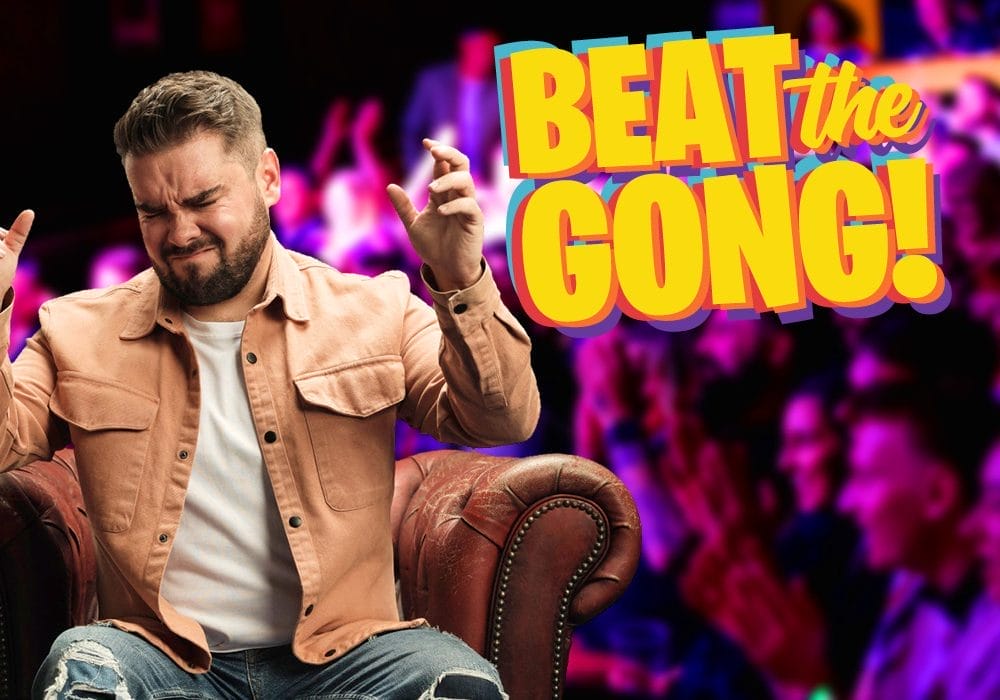 Comedian Adam Rowe, a white man with short dark hair, and a short dark beard, is grinning broadly while looking at the camera. To his right is the Beat the Gong logo.