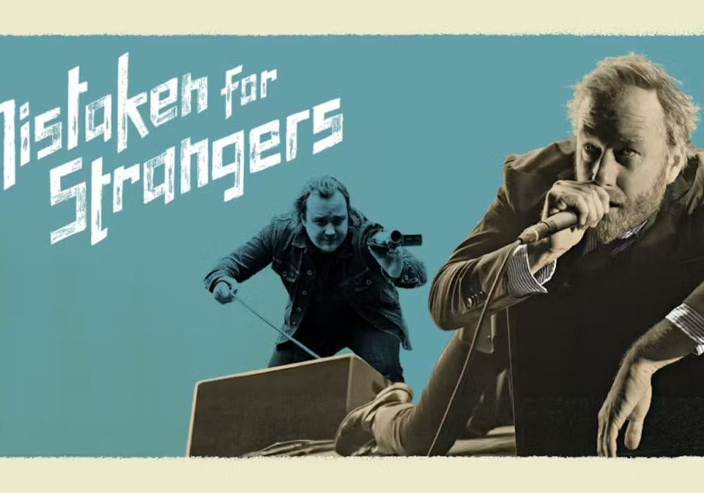 The singer Matt Berninger lounges to the right of the image, holding a microphone to his mouth. Behind him, the filmmaker Tom Berninger holds a handheld video camera. To the left of both men are the words Mistaken for Strangers.