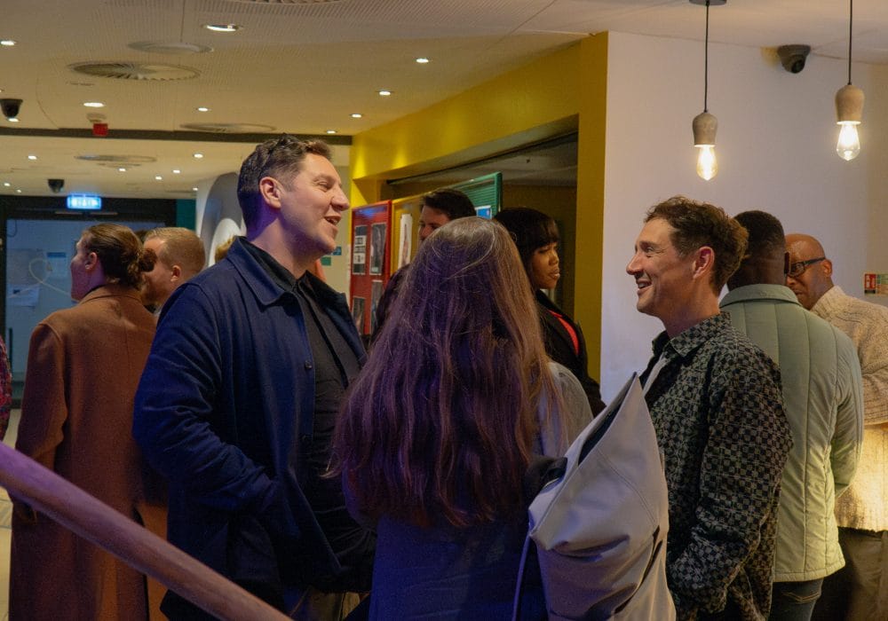 Three people stand chatting in a crowded room.