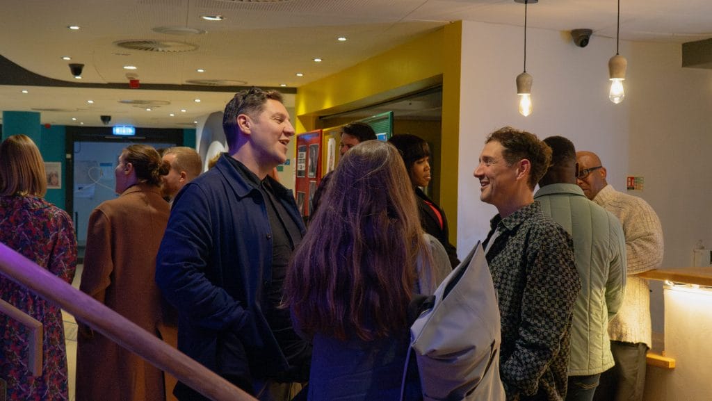 Three people stand chatting in a crowded room.