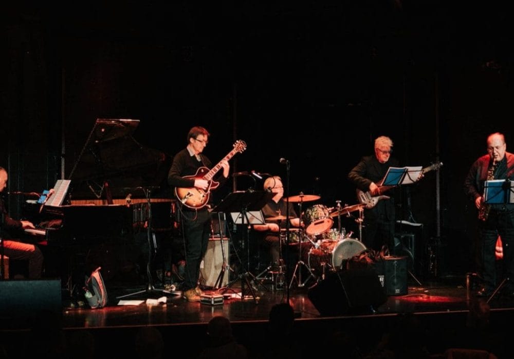 A five piece jazz band perform on stage to a crowd