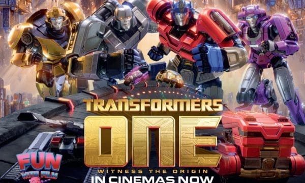 Four colourful Transformers robots are in the centre of the image, behind them is a futuristic cityscape. In front of them in metallic gold lettering are the words Transformers One: Witness the origin.