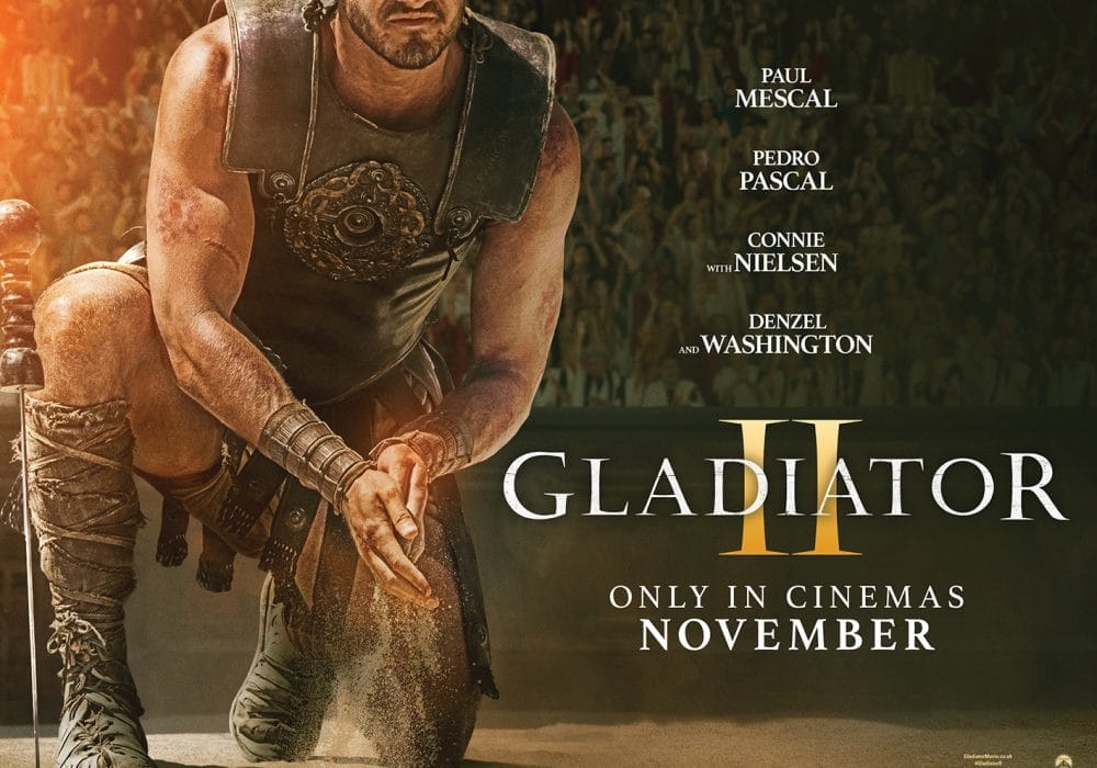 A roman gladiator kneels on sand, he is rubbing sand between his hands, his face is not visible. To the right of him is the title Gladiator II