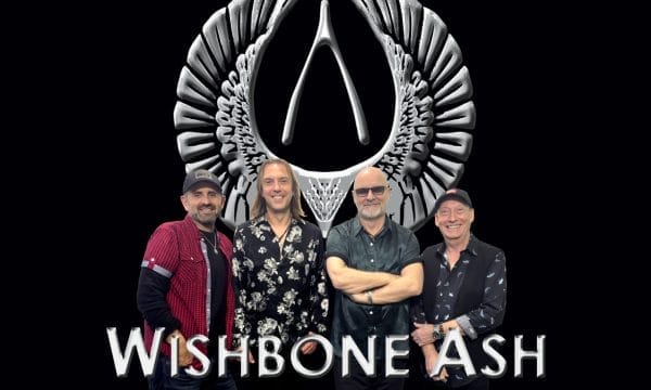 Four members of the band Wishbone Ash stand in front of a silver Wishbone Ash logo. Text reads: Wishbone Ash 2025 UK Tour