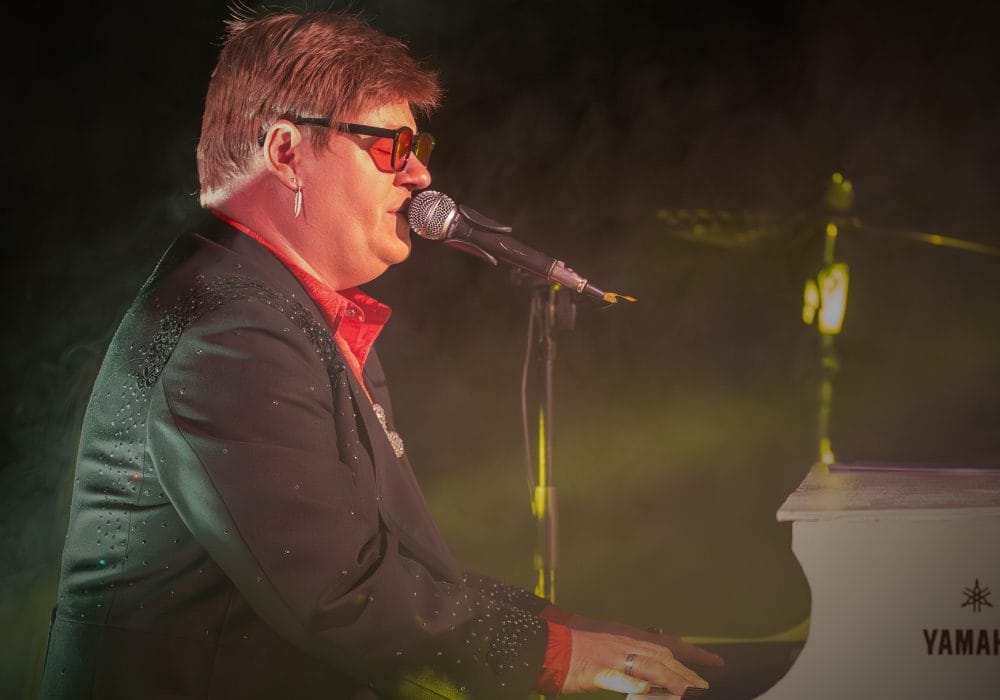 Elton Joel sits at a piano singing