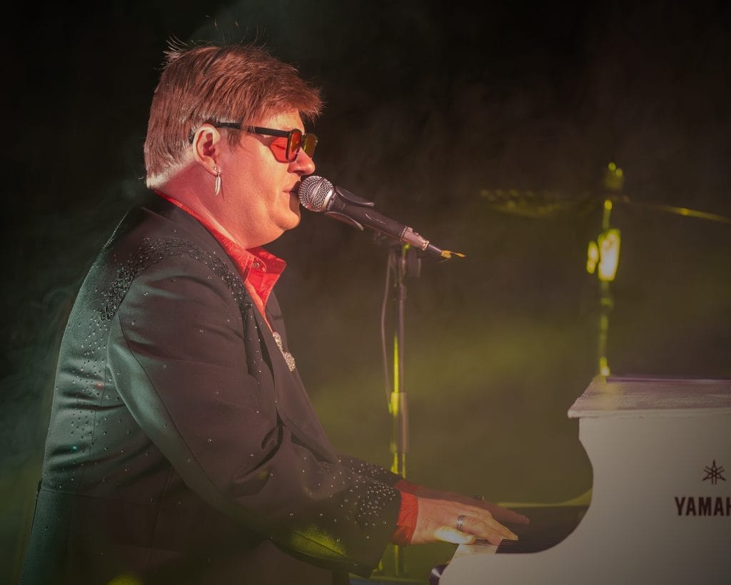 Elton Joel sits at a piano singing