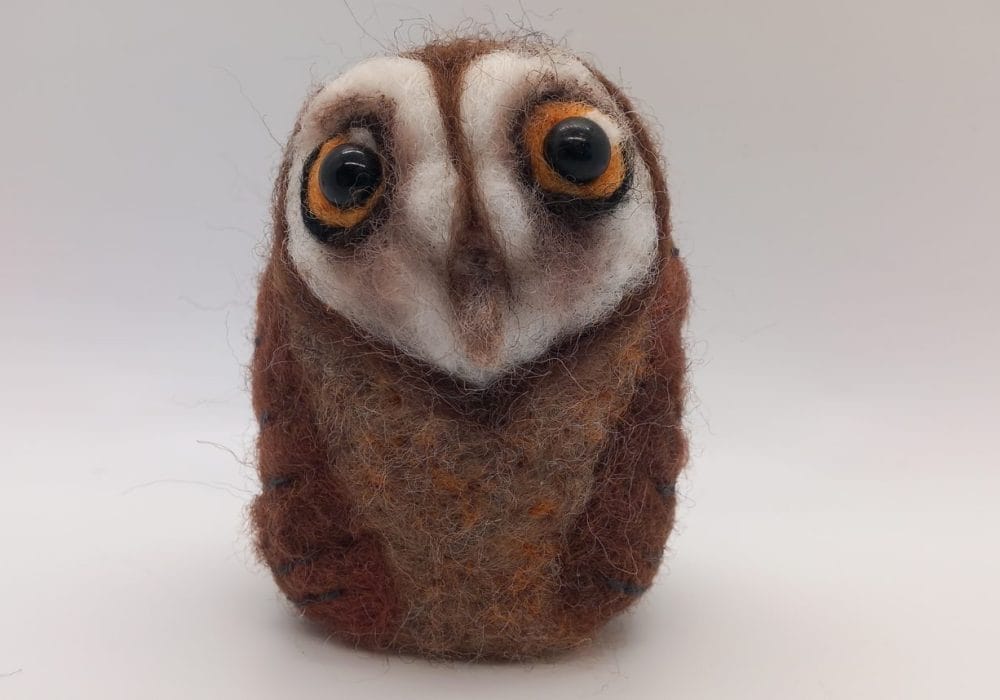 A round needle felted barn owl, with large yellow eyes.