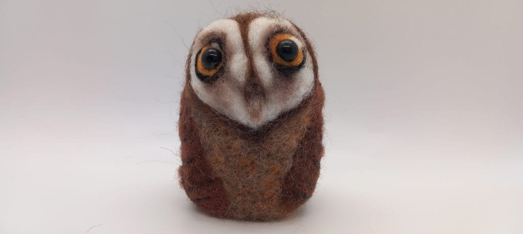 A round needle felted barn owl, with large yellow eyes.