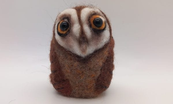 A round needle felted barn owl, with large yellow eyes.