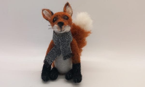 A needle felt fox, wearing a grey scarf.