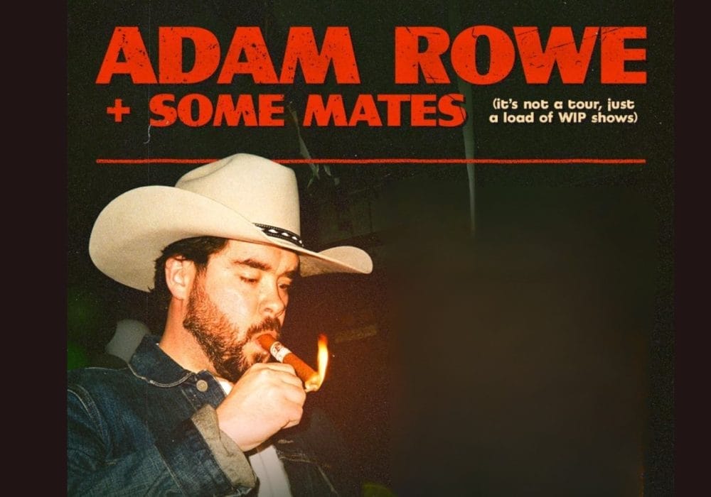A man with beard wearing a white cowboy cat and is lighting a cigar