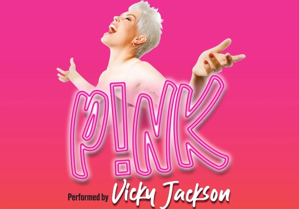 a promotional poster for a tribute show to the artist Pink. The poster features: A bright pink background The text "THE WORLD'S NO.1 TRIBUTE TO" at the top A large neon-style "P!NK" logo in the centre "Performed by Vicky Jackson" at the bottom The image shows a performer with short blonde/white hair in a pose reminiscent of Pink's energetic performance style, with arms outstretched against the vibrant pink backdrop.