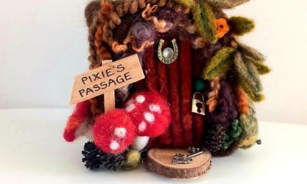 An Image of a needle felt wooden door with mushroom and leaves decorating its boarder, these are also needle felted.