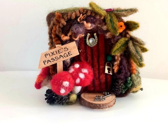 An Image of a needle felt wooden door with mushroom and leaves decorating its boarder, these are also needle felted.