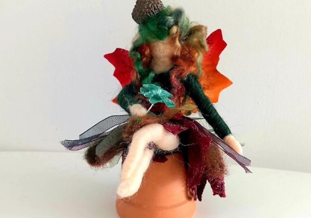 An image of a needle felted fairy sitting on top of a ceramic plant pot.