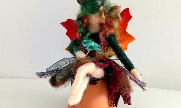 An image of a needle felted fairy sitting on top of a ceramic plant pot.