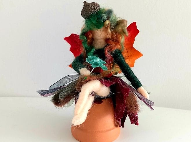 An image of a needle felted fairy sitting on top of a ceramic plant pot.