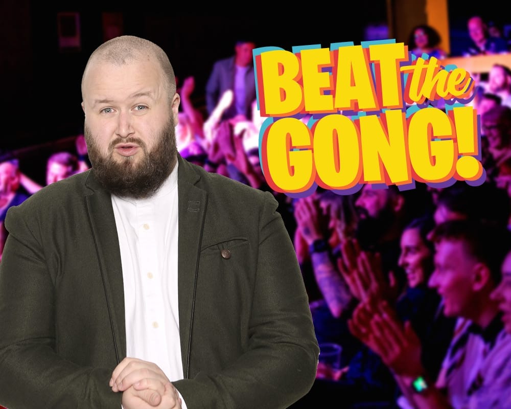 Comedian Freddy Quinne standing to the right of an animated Beat the Gong logo.