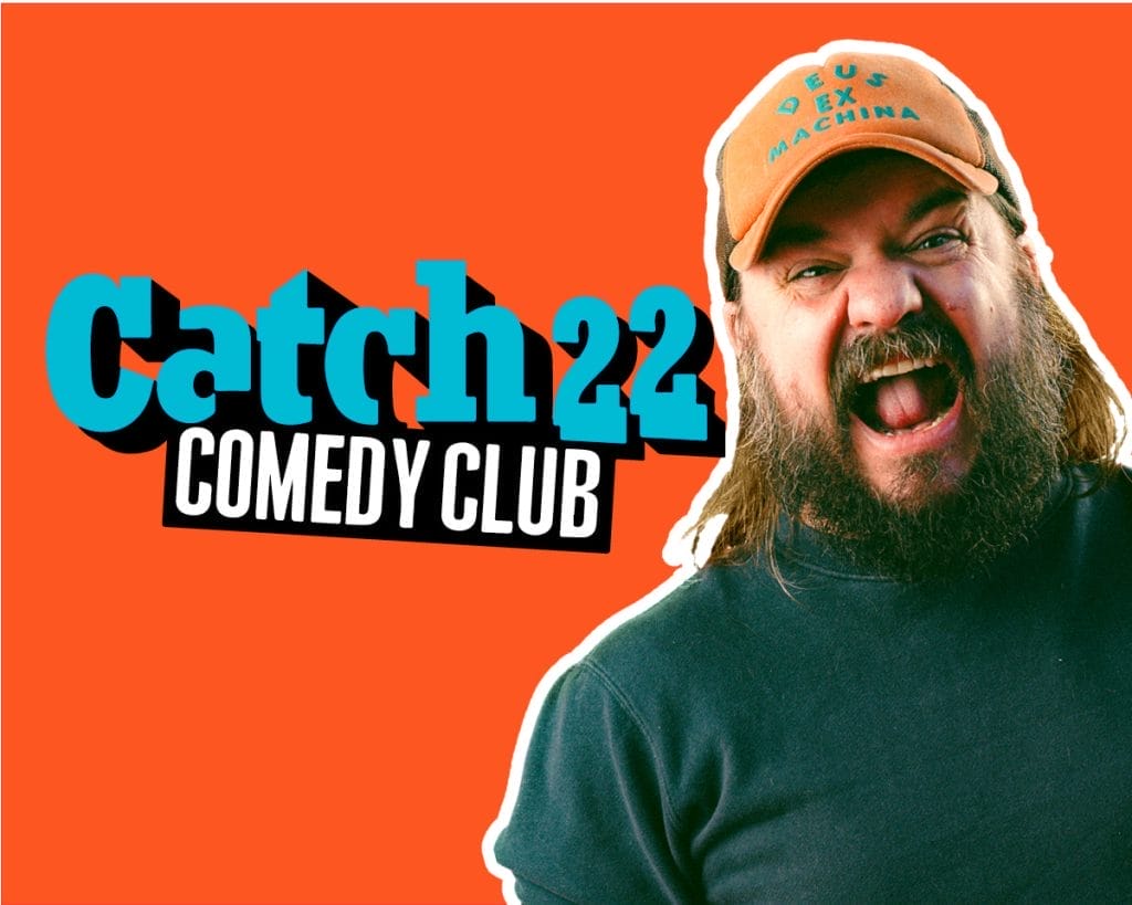 a promotional header for "Catch22 Comedy Club" with a bright orange background. The club's name appears in turquoise and white letters on the left side. On the right is a bearded man with long hair wearing an orange cap that reads "DEUS EX MACHINA" and a dark shirt. He appears to be laughing or shouting enthusiastically with his mouth open wide.