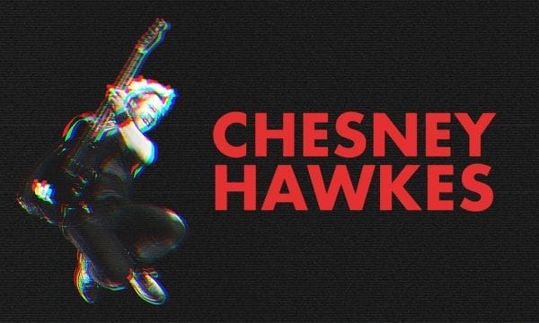 An image with red writing that reads 'Chesney Hawkes' to the left is a man mid-air holding a guitar. There is an glitch effect which makes the black and white image have blurred colours of red and blue surrounding it.