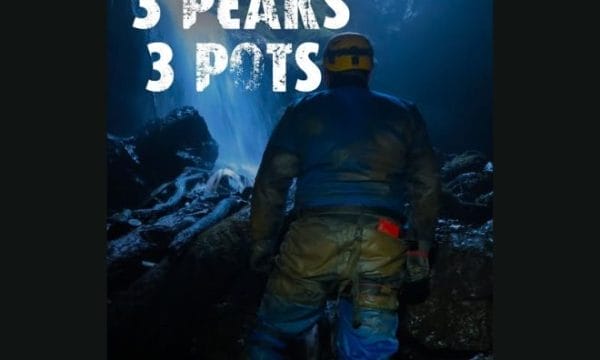 An image of a man in a hard hat and other caving gear, walking towards a cave opening. In the top of the screen there is a white title saying '3 peaks 3 pots'