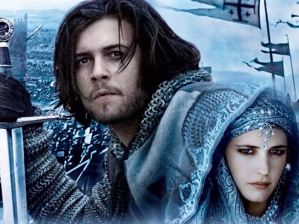 The image shows two people in medieval attire with a backdrop of what looks like a battlefield or city with an army. The scene depicts characters in historical costume with chainmail, a sword, and ornate Middle Eastern-inspired dress, set against what appears to be a medieval battlefield or fortress setting.