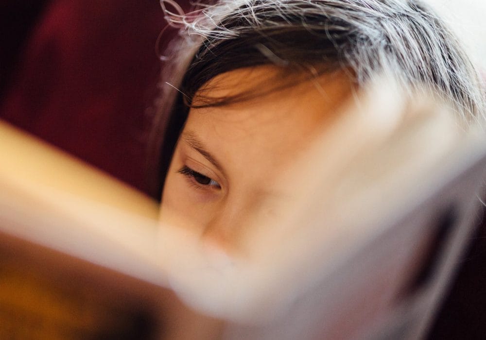 A close-up, intimate photo of someone reading, with warm lighting creating a cosy atmosphere. The person appears to be holding a book or document close to their face.