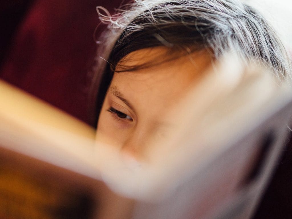 A close-up, intimate photo of someone reading, with warm lighting creating a cosy atmosphere. The person appears to be holding a book or document close to their face.