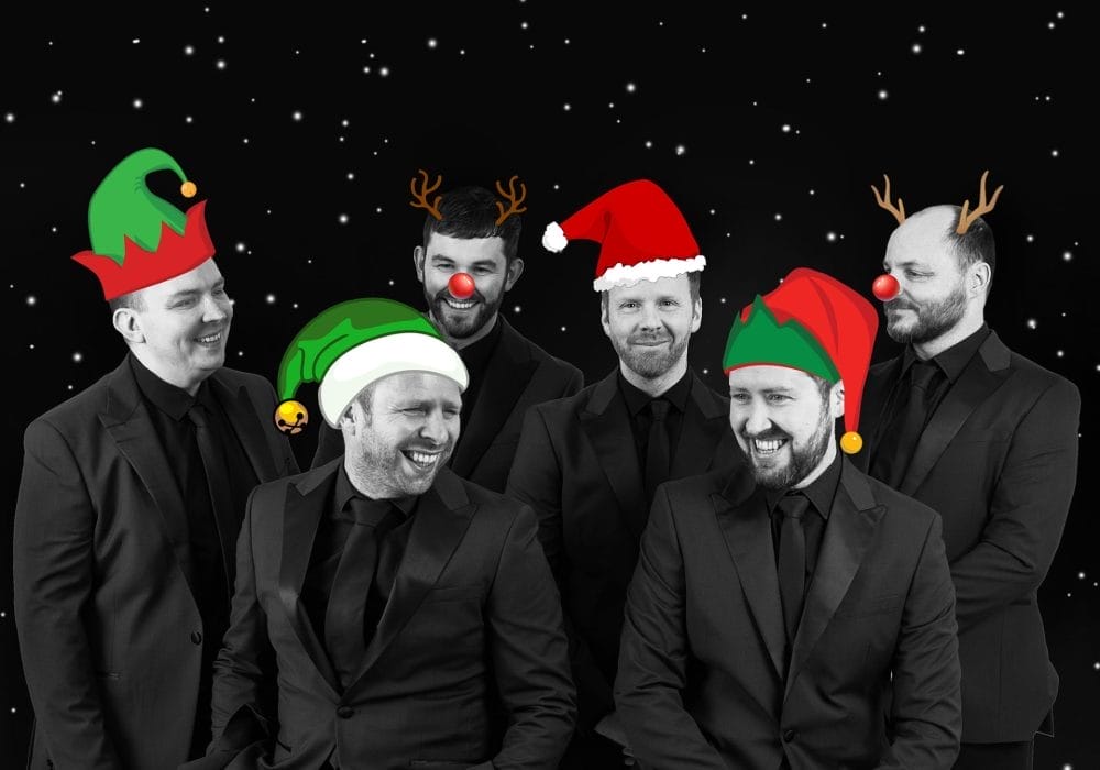 I can see a festive photo of six men in formal black suits against a starry night background, each wearing different Christmas accessories - elf hats, Santa hats, reindeer antlers, and red noses.
