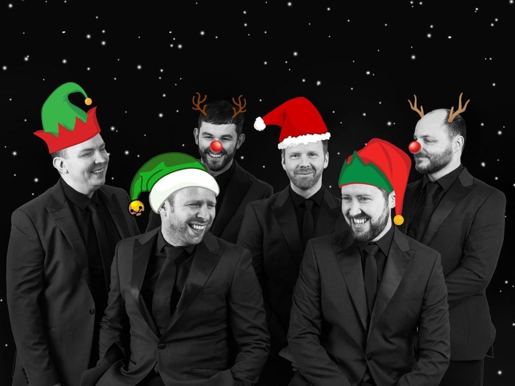 I can see a festive photo of six men in formal black suits against a starry night background, each wearing different Christmas accessories - elf hats, Santa hats, reindeer antlers, and red noses.