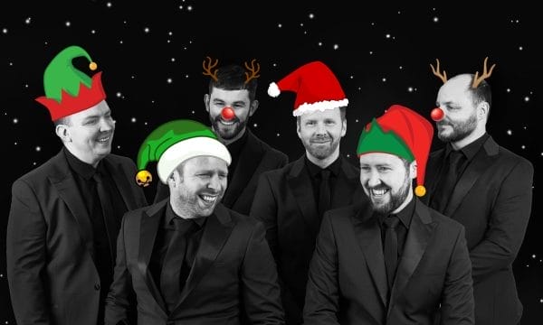 I can see a festive photo of six men in formal black suits against a starry night background, each wearing different Christmas accessories - elf hats, Santa hats, reindeer antlers, and red noses.
