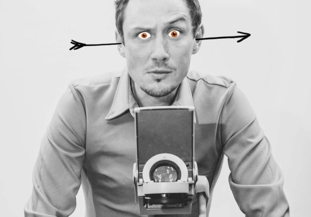 A black & white image of Scott Turnbull stood behind an overhead projector. He has an arrow through his ears and red cartoon eyes.
