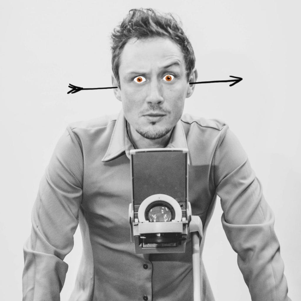A black & white image of Scott Turnbull stood behind an overhead projector. He has an arrow through his ears and red cartoon eyes.