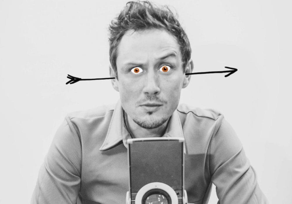 A black & white image of Scott Turnbull stood behind an overhead projector. He has an arrow through his ears and red cartoon eyes.