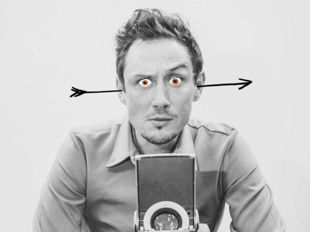A black & white image of Scott Turnbull stood behind an overhead projector. He has an arrow through his ears and red cartoon eyes.