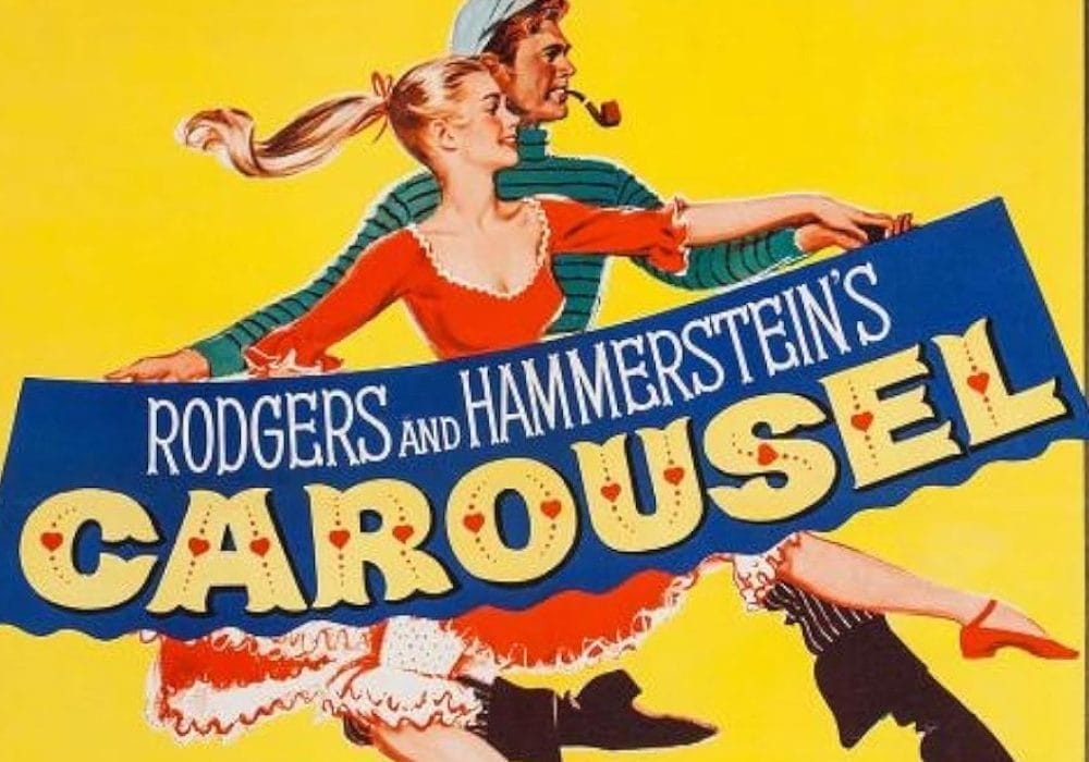 a bright yellow background with a man and woman in 1940s period costume. The woman wears a red dress with white trim and has blonde hair flowing in the wind. The man behind her wears a green and white striped shirt and a flat cap, smoking a pipe. They appear to be running or moving dynamically across the poster. The title "CAROUSEL" is displayed prominently in large, decorative letters with red heart symbols dotting the text. Above the title, "RODGERS AND HAMMERSTEIN'S" appears in white text on a blue banner.