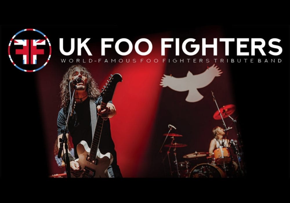 a live performance with a guitarist/vocalist in the foreground and a drummer in the background, along with their branding that includes the Union Jack flag incorporated into their logo.