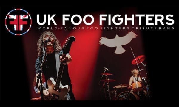 a live performance with a guitarist/vocalist in the foreground and a drummer in the background, along with their branding that includes the Union Jack flag incorporated into their logo.