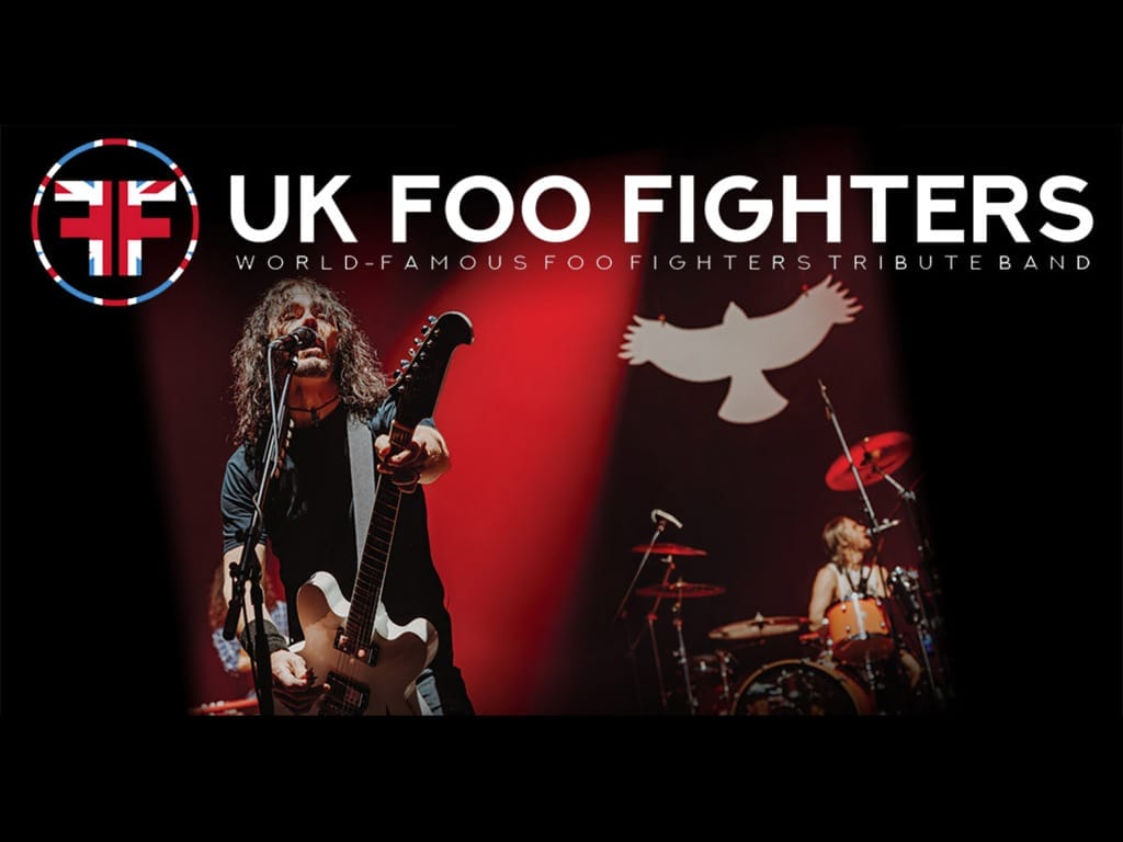 a live performance with a guitarist/vocalist in the foreground and a drummer in the background, along with their branding that includes the Union Jack flag incorporated into their logo.
