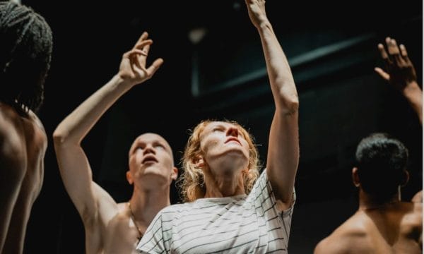 A group of people in a dance studio raises their hands, showcasing enthusiasm and energy during a dance session.