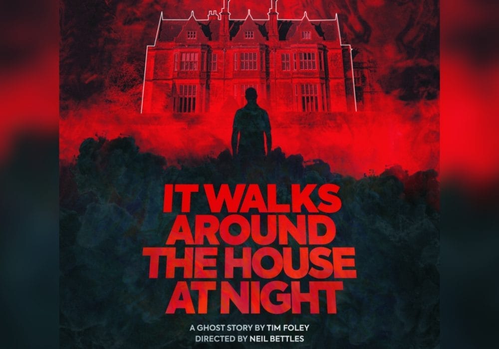 A dramatic horror-style poster featuring a silhouetted figure standing before a large, imposing mansion or estate house. The entire scene is bathed in deep red lighting, creating an ominous atmosphere. The building appears to be a grand English country house with multiple chimneys, ornate windows, and classical architecture. Bold red text at the bottom reads 'IT WALKS AROUND THE HOUSE AT NIGHT' against a dark, moody background with shadowy foliage in the foreground.