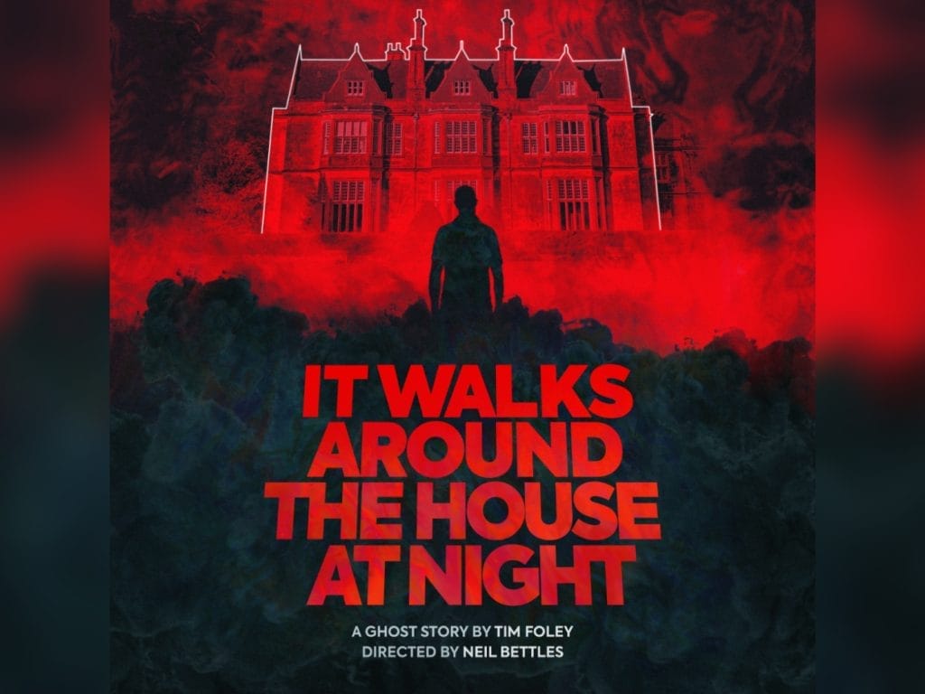 A dramatic horror-style poster featuring a silhouetted figure standing before a large, imposing mansion or estate house. The entire scene is bathed in deep red lighting, creating an ominous atmosphere. The building appears to be a grand English country house with multiple chimneys, ornate windows, and classical architecture. Bold red text at the bottom reads 'IT WALKS AROUND THE HOUSE AT NIGHT' against a dark, moody background with shadowy foliage in the foreground.