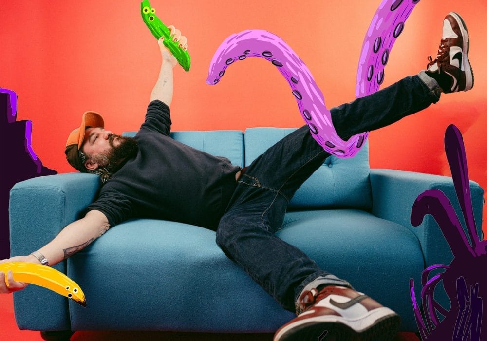 A person lying on a light blue sofa against a vibrant orange-red background, appearing to be grabbed by large purple tentacles with suction cups. They're holding a green pickle-shaped object and wearing dark clothing with trainers. Yellow and purple tentacle-like shapes frame the scene, creating a surreal, playful composition that blends reality with fantastical elements.