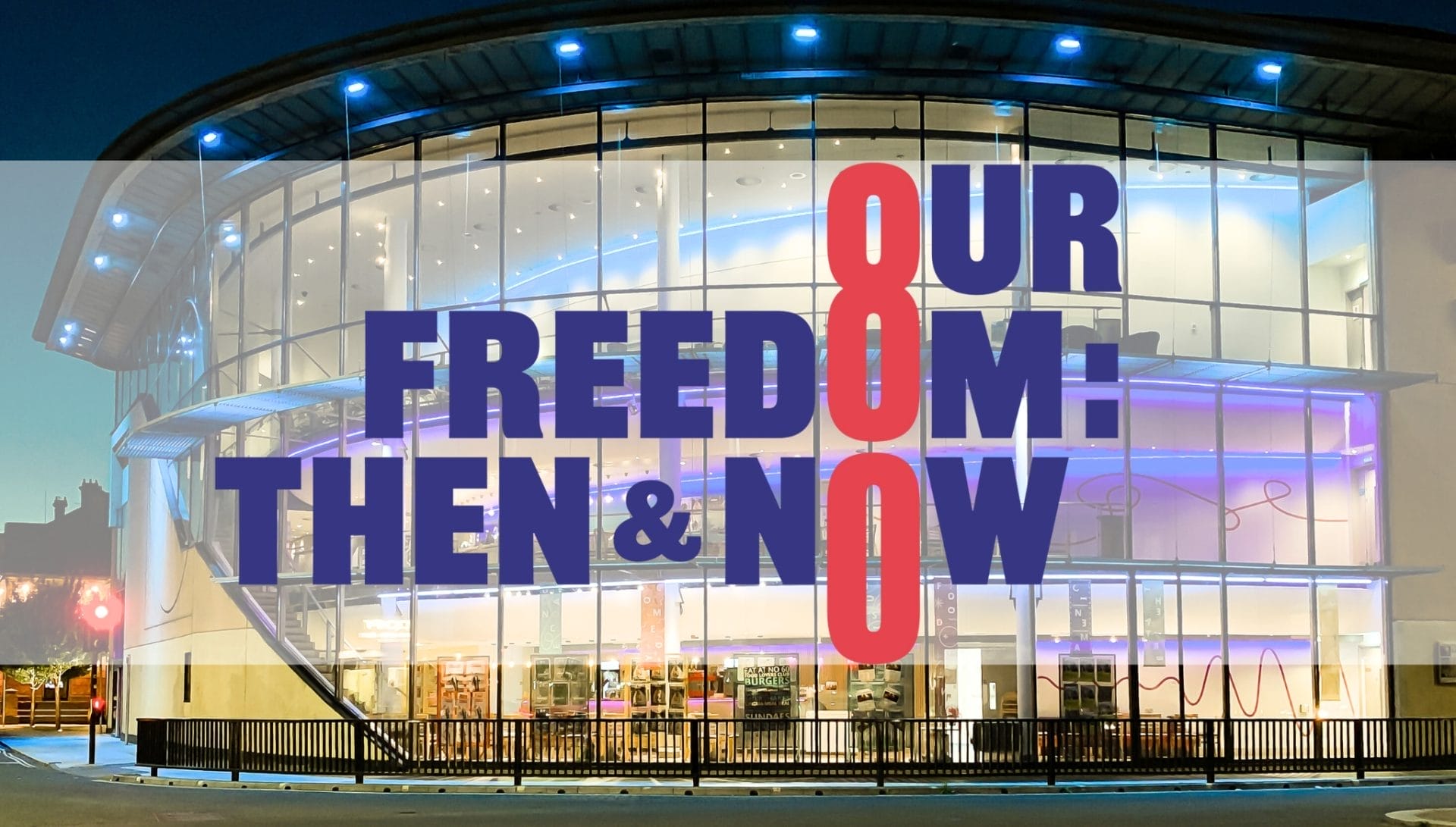 Modern building with large glass windows lit up at night, overlaid with text reading "OUR FREEDOM: THEN & NOW."