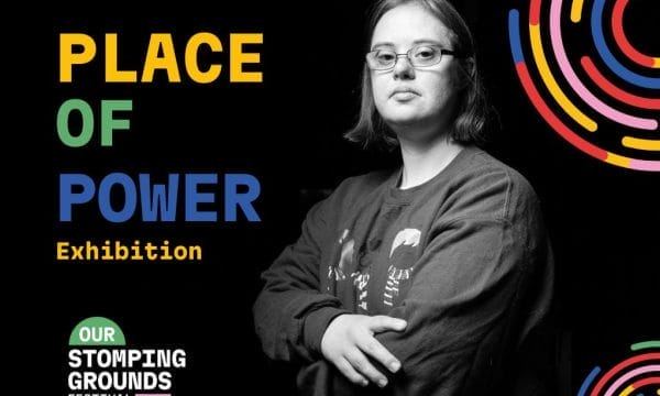 A monochrome image of a young person wearing glasses, arms folded. They have a neutral expression on their face.