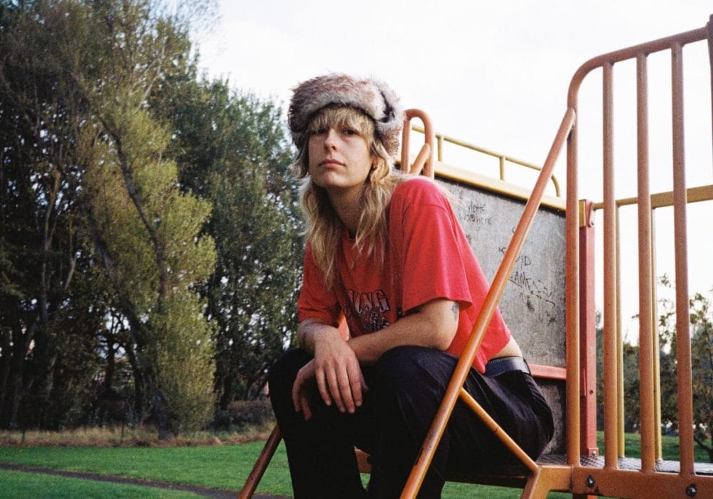 Melanie sits on steps to a play area in a park seating looking at you
