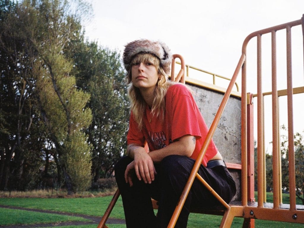 Melanie sits on steps to a play area in a park seating looking at you