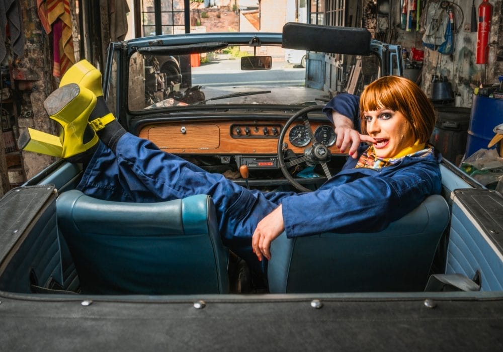 A car mechanic wearing blue overalls sat across the seats of a shell of a car